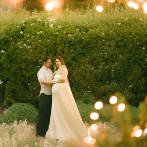 An image capturing the elegance of a radiant mother-to-be in a flowing ivory maternity dress, delicately cradling her baby bump, while strolling amongst a garden adorned with blooming roses and twinkling fairy lights